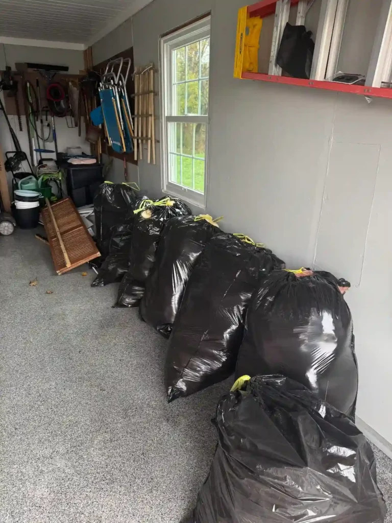 Black trash bags lined up inside a garage during a residential junk removal pickup in Elmira, NY.