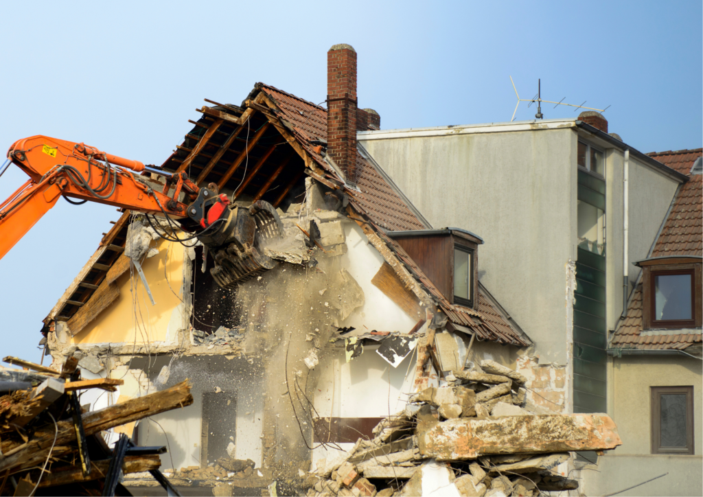 Orange excavator tearing down a two-story house during demolition and structure removal in Painted Post, NY